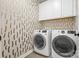 Bright laundry room with white washer and dryer, modern wallpaper, and white cabinets at 921 E 36Th St, Charlotte, NC 28205