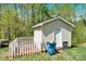 A small storage shed in the wooded backyard has a white picket fence at 2315 Collins Dr, Albemarle, NC 28001