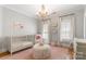 Bright Bedroom featuring a chandelier, crib, accent chair, and shuttered windows at 3819 Gleneagles Rd, Charlotte, NC 28210
