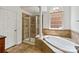 Bathroom with a tub, a glass shower, tiled walls, and a window overlooking a landscaped yard at 7302 Yellowhorn Trl, Waxhaw, NC 28173