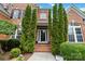Inviting front entrance with a glass door, brick steps, and manicured landscaping, enhanced by tall evergreens at 7302 Yellowhorn Trl, Waxhaw, NC 28173