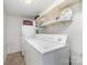 Functional laundry room with white washer and dryer, supplemented by shelving for storage and supplies at 5807 Sharon Rd # A, Charlotte, NC 28210