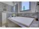 A soaking tub features beautiful tile surround and a large window in this contemporary bathroom at 1306 Kings Bottom Dr, Fort Mill, SC 29715
