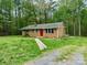 Brick home with a chimney, red door, surrounded by a lush green lawn and dense trees at 181 Canipe Rd, Dallas, NC 28034