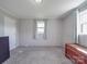 A well-lit bedroom with grey carpet and paneled walls, with 2 windows, soft blue curtains, a chest, and a three-drawer dresser at 1315 Holshouser Rd, Rockwell, NC 28138