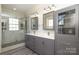 Bathroom featuring a glass shower with stone pebble floor, dual sinks, and gray cabinets at 2015 Dilworth E Rd, Charlotte, NC 28203