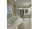 Luxurious bathroom with soaking tub, glass shower, white tile and countertops, and plantation shutters at 9113 Oak Bluff Ct, Waxhaw, NC 28173