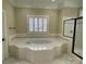 Spacious bathroom with soaking tub, glass shower, white tile, and a window with plantation shutters at 9113 Oak Bluff Ct, Waxhaw, NC 28173