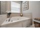 Corner soaking tub bathed in natural light, framed by neutral tile, offers a serene retreat for relaxation and comfort at 15613 Troubadour Ln, Huntersville, NC 28078