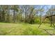 A spacious backyard featuring mature trees, lush green grass, and a charming, rustic wooden swing set for added enjoyment at 2120 Turtle Point Rd, Charlotte, NC 28262