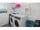 This laundry room has a white washer and dryer with white walls and shelves at 1077 Hearth Sw Ln, Concord, NC 28025