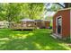 Landscaped backyard featuring a brick house, wooden deck, green grass, with a red storage shed at the edge of yard at 2721 Albany Ln, Charlotte, NC 28205