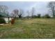 Exterior backyard view with overgrown grass and damaged furniture on a cloudy day, requiring extensive maintenance at 2702 W Stage Coach Trl, Shelby, NC 28150