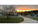 Picturesque street view with mature trees, a curved driveway, and a beautiful sunrise backdrop at 557 Luther Dr, Iron Station, NC 28080