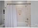 A bathtub with a white tile surround and shower, with a white shower curtain rod and white curtain at 3228 E Ford Rd, Charlotte, NC 28205