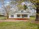 Charming white cottage with metal roof, black shutters, and inviting front porch surrounded by mature trees at 589 Lippard Farm Rd, Statesville, NC 28625