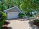 A two-car garage with a concrete driveway, white trim, and surrounded by mature trees and manicured landscaping at 15323 Barnsbury Dr, Huntersville, NC 28078