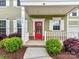 Close-up of a vibrant red front door with white trim, surrounded by lush landscaping and charming details at 15747 Reynolds Dr, Indian Land, SC 29707