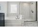 Bathroom featuring a bathtub, shower, and dark fixtures surrounded by white marble tile at 2533 Ensemble Ct, Charlotte, NC 28262