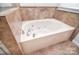 Close-up of a luxurious soaking tub with jets and a modern faucet, surrounded by travertine tile at 2415 Tory Oak Pl, Matthews, NC 28105