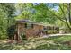 View of the single-story brick home surrounded by lush trees and landscaping on a well-manicured lawn at 6325 Elmwood Cir, Charlotte, NC 28214