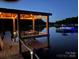 Lakeside covered dock with table and chairs is illuminated at night with string lights at 6778 Emerald Isle Dr, Sherrills Ford, NC 28673