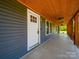 Covered front porch with a wood ceiling, a white door, and views of the surrounding greenery at 3546 Mount Pleasant N Rd, Concord, NC 28025
