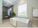 Bright bathroom featuring a soaking tub, glass enclosed shower, and a large window for natural light at 100 Verbena Ct, Weddington, NC 28173