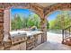Covered outdoor kitchen with stone counter, grill, and refrigerator overlooking pool with rock waterfall at 17909 Golden Meadow Ct, Davidson, NC 28036