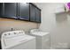 Bright laundry room with Whirlpool washer and dryer, overhead cabinets, and shelving for storage at 3216 Moss Ln, Charlotte, NC 28206