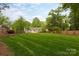 Wide view of the lush backyard with a large lawn, mature trees, and a welcoming deck at 6701 Highbrook Dr, Charlotte, NC 28212