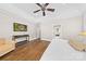 Well-lit bedroom with hardwood floors, ceiling fan, mounted TV and a comfortable chair at 7181 Windy Ridge Dr, Iron Station, NC 28080