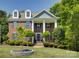 A brick two-story home with white pillars and blue shutters surrounded by green trees and a beautifully landscaped front yard at 9810 Daufuskie Dr, Charlotte, NC 28278