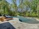 Private backyard featuring a curved pool, stone patio, lounge chairs, and lush mature trees at 712 Chase Ct, Fort Mill, SC 29708
