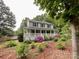 Inviting two-story home with a charming front porch and lush landscaping with blooming pink flowers and mature trees at 2214 Cannonade Ct, Matthews, NC 28105