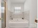 Bright bathroom featuring a large soaking tub with tile surround and a window for natural light at 14457 Adair Manor Ct, Charlotte, NC 28277