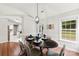 Bright dining room with dark wood floors, a modern chandelier, and views of the green backyard through multiple windows at 13324 Kintyre Ct, Matthews, NC 28105