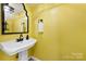 Cheerful half bath featuring a pedestal sink, decorative mirror, and vibrant yellow walls at 4605 Hedgemore Dr # I, Charlotte, NC 28209