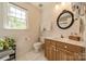 Bright bathroom features a vanity with wood cabinets, white countertop, decorative mirror, and a window at 14926 Chilgrove Ln, Huntersville, NC 28078