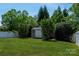 Large backyard with a storage shed, surrounded by mature trees and a white fence at 1004 Toquima Trl, Monroe, NC 28110