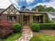 Inviting front porch with brick flooring, supported by green pillars and surrounded by manicured shrubbery at 1596 Clayton Dr, Charlotte, NC 28203