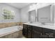 Bright bathroom boasts a double sink vanity, soaking tub with tile surround, and a large mirror at 3245 Major Samuals Way, Charlotte, NC 28208
