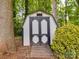 Wooden storage shed with double doors nestled in a serene, wooded area with lush green foliage at 8623 Cedar Hollow Ln, Huntersville, NC 28078