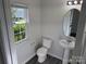 Well-lit half bathroom features a pedestal sink, toilet, and a window overlooking the yard at 2815 Cartesian Dr, Charlotte, NC 28214