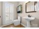 Well-lit bathroom with a pedestal sink, modern toilet, decorative mirror, and window with plantation shutters at 2710 Providence Spring Ln, Charlotte, NC 28270