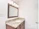 Bathroom vanity with granite countertop, wood cabinets, and decorative mirror with lighting at 6631 Vlosi Dr, Charlotte, NC 28226