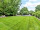 Expansive backyard boasts lush green grass, mature trees, a sports court, and a patio with fireplace and custom seating at 7809 Greenfield Dr, Charlotte, NC 28270