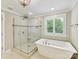 Bright bathroom featuring a glass shower, a white tub, and a window at 7809 Greenfield Dr, Charlotte, NC 28270