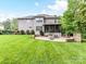 Back exterior view showcasing a large home, covered patio, custom stone patios, lush lawn, and manicured landscaping at 7809 Greenfield Dr, Charlotte, NC 28270