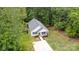 Aerial view of a quaint home featuring a gray roof, white siding, front porch, deck, and driveway surrounded by lush trees at 409 Woodcrest Ln, Albemarle, NC 28001
